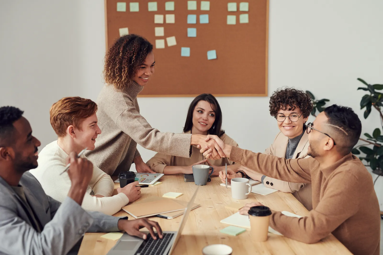 Equipo reunido alrededor de una mesa de trabajo mientras una persona presenta ideas en una pizarra